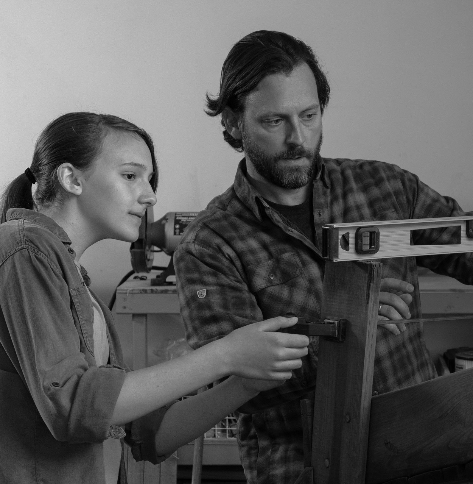 Man using a level on a wood project and a young woman helping adjust.