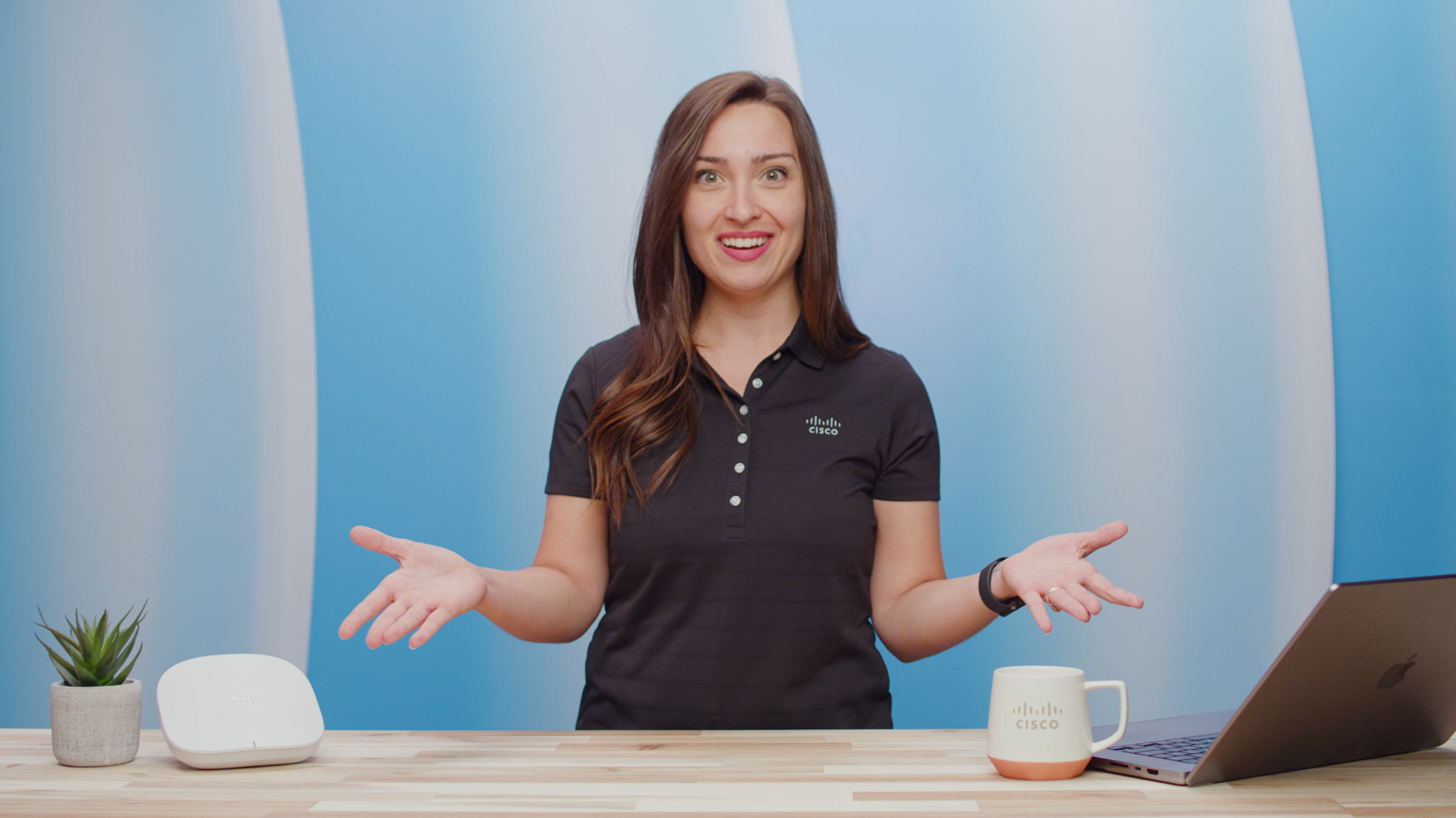 A young female standing behind a desk, she is talking and has her hands in front of her.